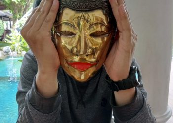 Seorang anak sedang memakai topeng Mina Tani.