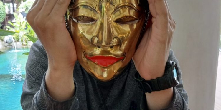 Seorang anak sedang memakai topeng Mina Tani.